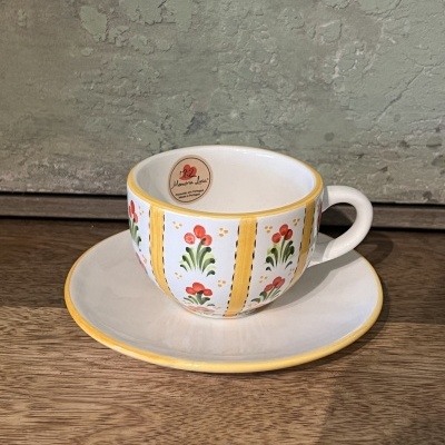 Chávena de cerâmica branca com padrão floral vermelho e verde e riscas amarelas no pires