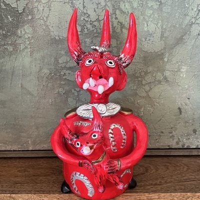 Estatueta vermelha com três chifres e detalhes brancos e pretos segurando figura pequena semelhante