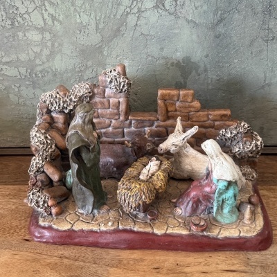 Presépio em resina com figuras de Maria, José, Menino Jesus, boi e burro em cenário de pedras sobre base vermelha