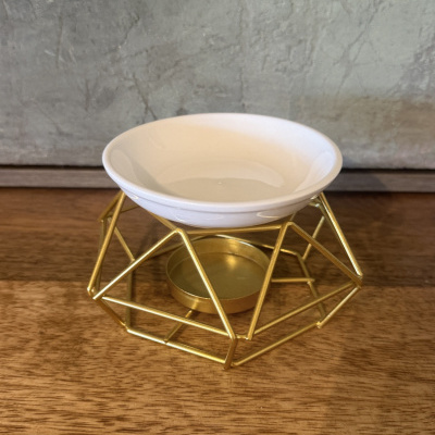 Suporte dourado geométrico para velas com tigela branca em cerâmica sobre superfície de madeira.