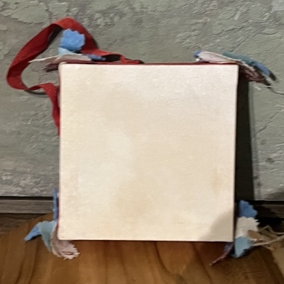 Mala quadrada de tecido bege com alça vermelha e detalhes azuis