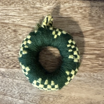 Anel de lã verde e amarela com padrão quadriculado sobre madeira