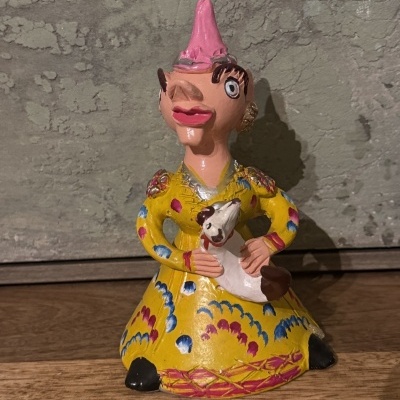 Estátua cerâmica colorida de mulher com vestido amarelo e cão branco.