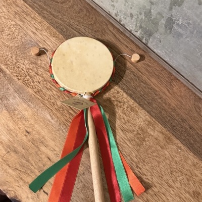 Pandeireta com fitas coloridas vermelhas, verdes e laranja sobre mesa de madeira