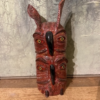 Máscara decorativa de madeira vermelha com olhos amarelos e pretos e narizes pretos