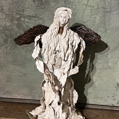 Estátua de anjo com asas castanhas e vestido branco sobre base retangular