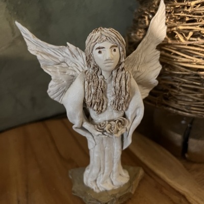 Estatueta de anjo cerâmico branco com asas e cabelo detalhado sobre superfície de madeira