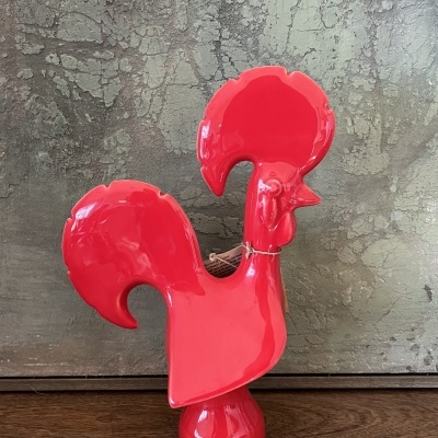 Figurinha de galo vermelha brilhante sobre madeira com fundo texturizado cinza.