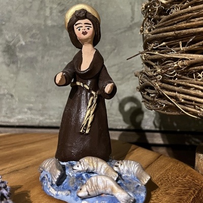 Estátua de santo em cerâmica com peixes na base sobre madeira