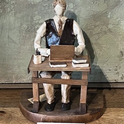 Escultura decorativa de homem a trabalhar num escritório com laptop e acessórios sobre mesa de madeira