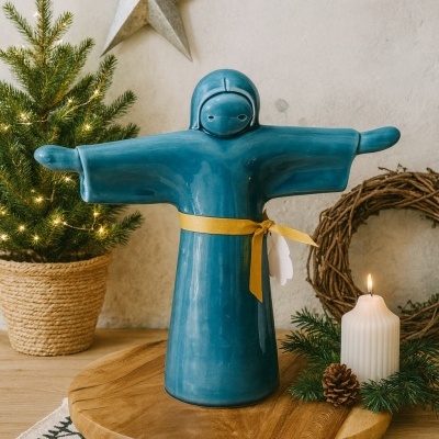 Estatueta azul em cerâmica com cinto amarelo sobre base de madeira com vela e enfeites de Natal