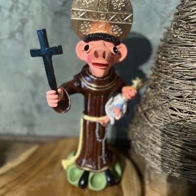 Figura de cerâmica de santo com crucifixo e Menino Jesus ao lado de decoração de fibra natural