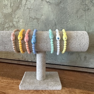 Pulseiras coloridas de contas com contas centrais em forma de peixe exibidas em suporte cinzento.