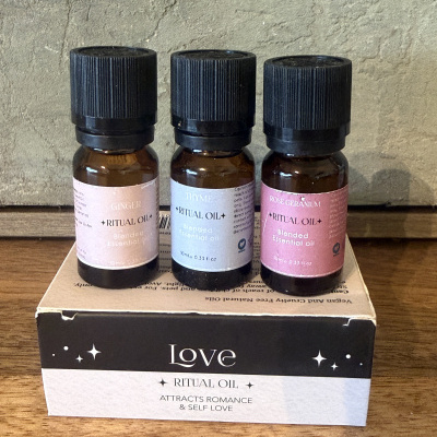 Três frascos de óleos essenciais de diferentes aromas em frascos âmbar com tampas pretas sobre uma caixa com texto Love Ritual Oil