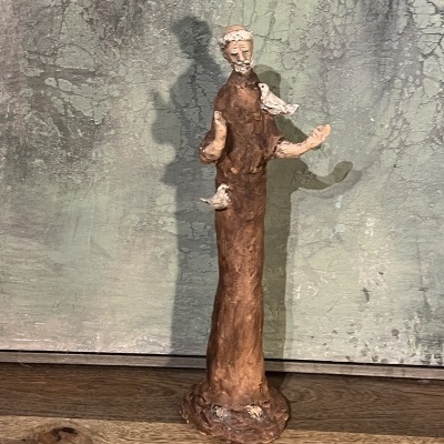 Estátua cerâmica de figura humana com pombo, sobre madeira com fundo texturizado