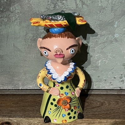 Figura decorativa colorida em cerâmica com vestido verde e chapéu com objetos amarelos e vermelhos