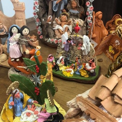 Presépio com figuras coloridas em cerâmica e barro, decorado com elementos naturais, exposto sobre mesa de madeira