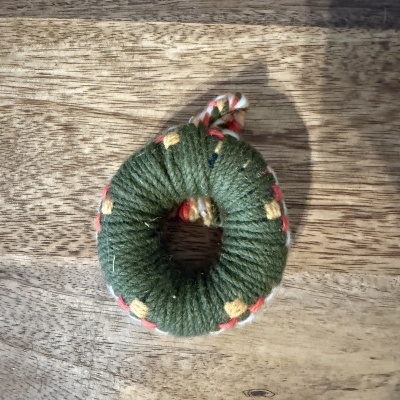 Anel decorativo em tecido verde com pontos amarelos sobre madeira clara.