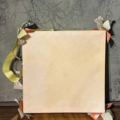 Caixa quadrada bege com cantos de tecido colorido numa superfície de madeira