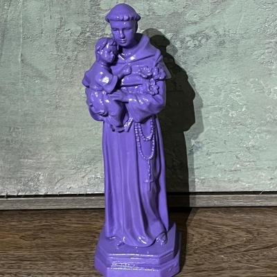 Estatueta roxa de São Francisco de Assis com Menino Jesus e terço, sobre superfície de madeira