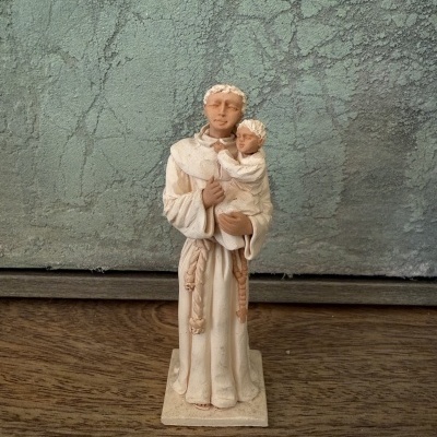 Estátua religiosa de homem com criança em cor bege sobre superfície de madeira com parede texturada ao fundo