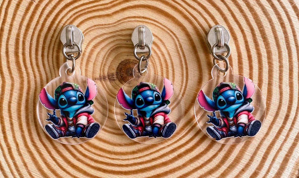 Três chaveiros redondos transparentes com personagem Stitch vestido, pendurados em ganchos sobre madeira