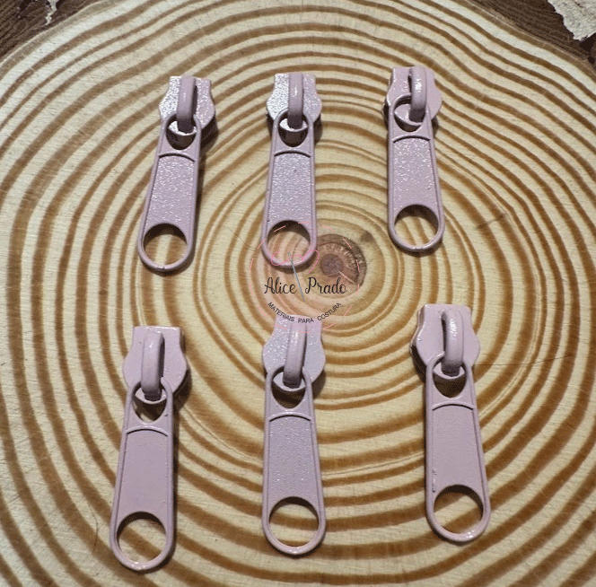Seis puxadores de zíper rosa claro em superfície com padrão de anéis concêntricos