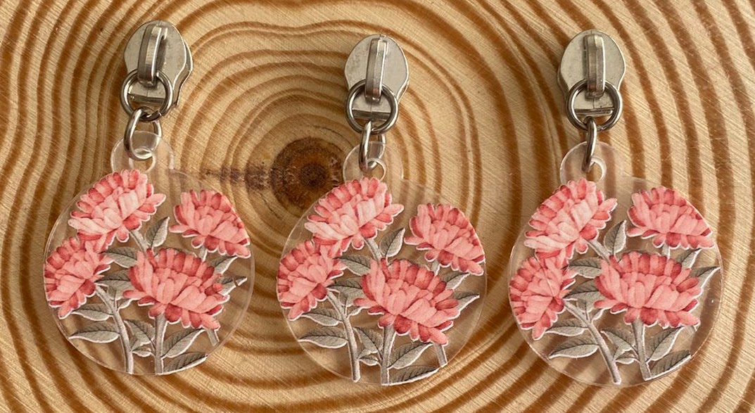 Três chaveiros redondos com flores cor-de-rosa em relevo em superfície de madeira