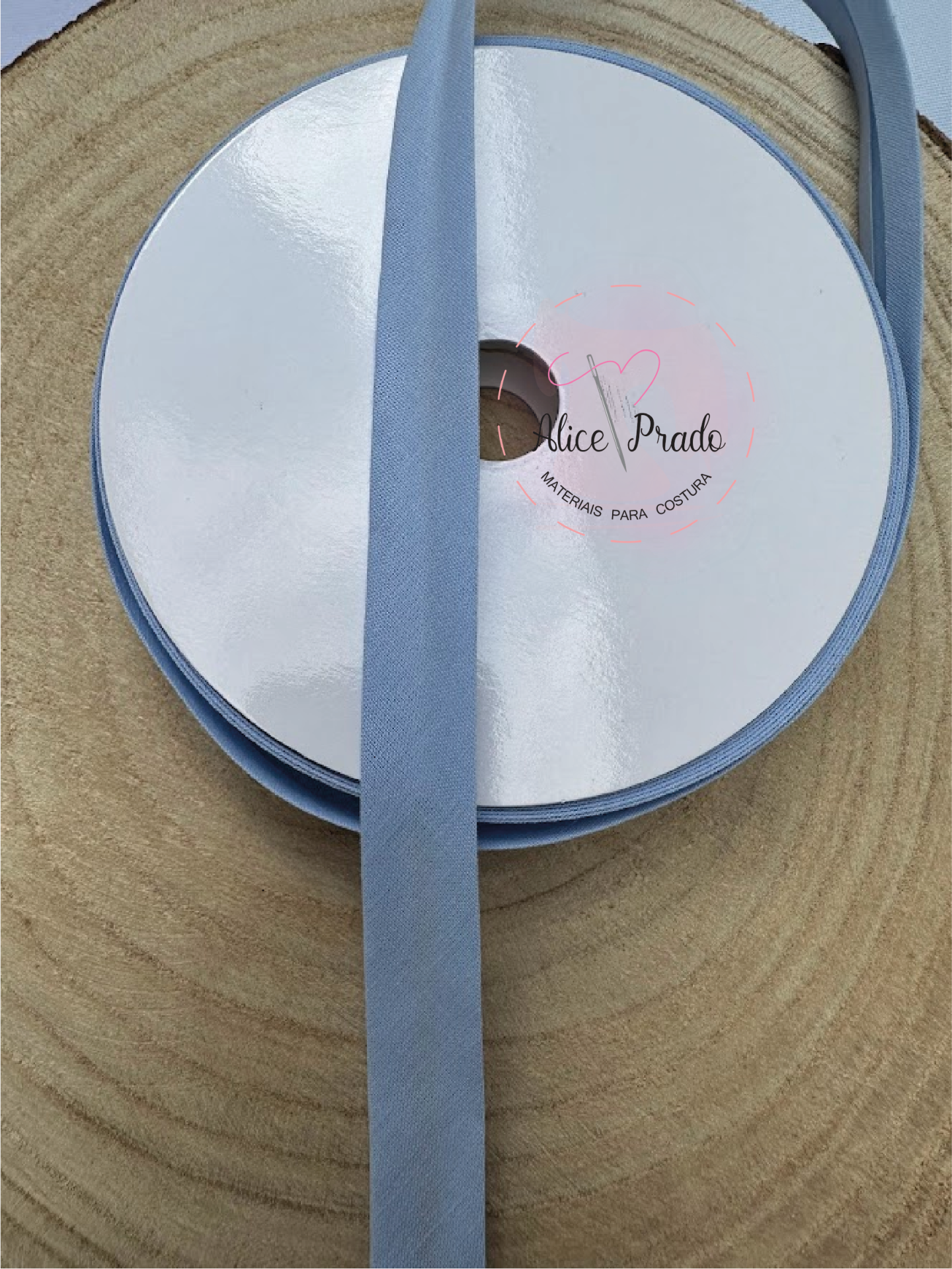 Rolo de fita de tecido azul claro com etiqueta branca sobre superfície de madeira redonda