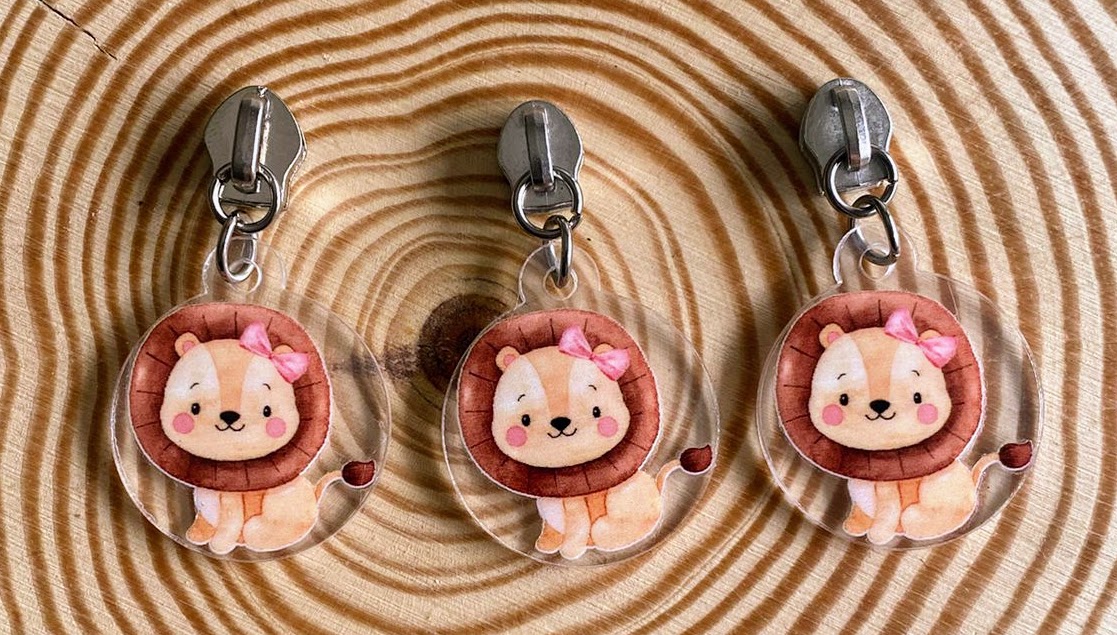 Três chaveiros de leão com laço rosa em fundo de madeira com anéis concêntricos