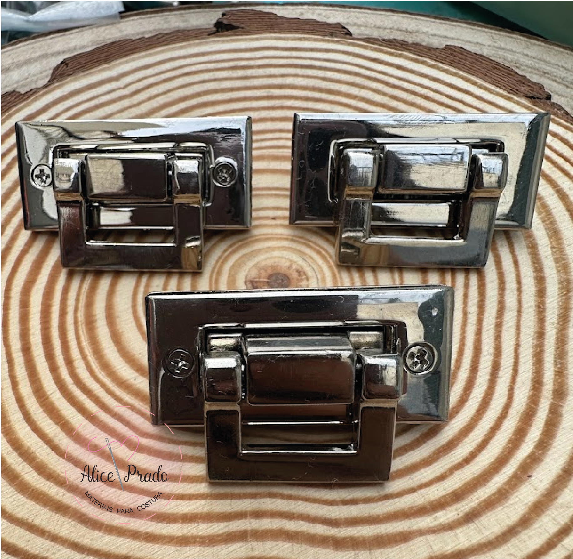 Três fechos metálicos prateados sobre superfície de madeira com padrão de anéis.