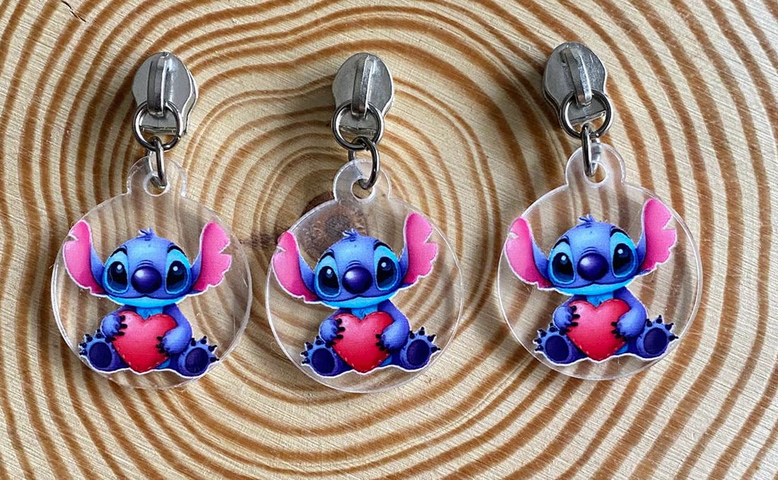 Três chaveiros transparentes com personagem Stitch segurando um coração vermelho sobre padrão espiral bege