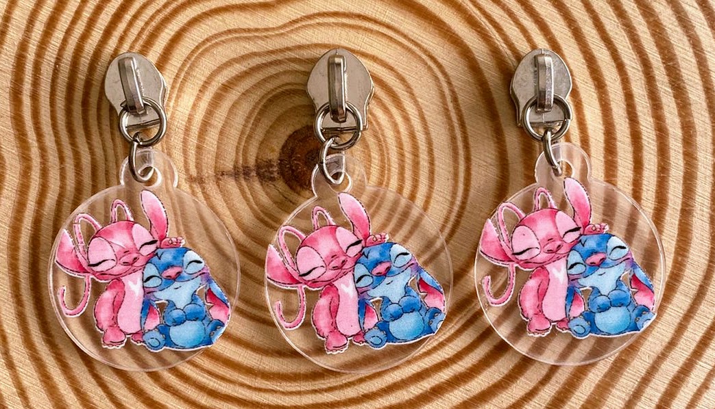 Três porta-chaves com desenho de coelho rosa e criatura azul abraçados em superfície de madeira.