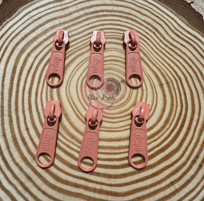 Seis puxadores de fecho éclair cor-de-rosa sobre superfície de madeira com anéis