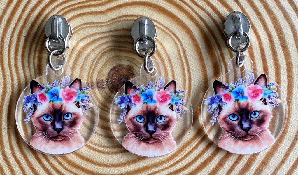 Três porta-chaves com rosto de gato e flores pendurados em superfície de madeira