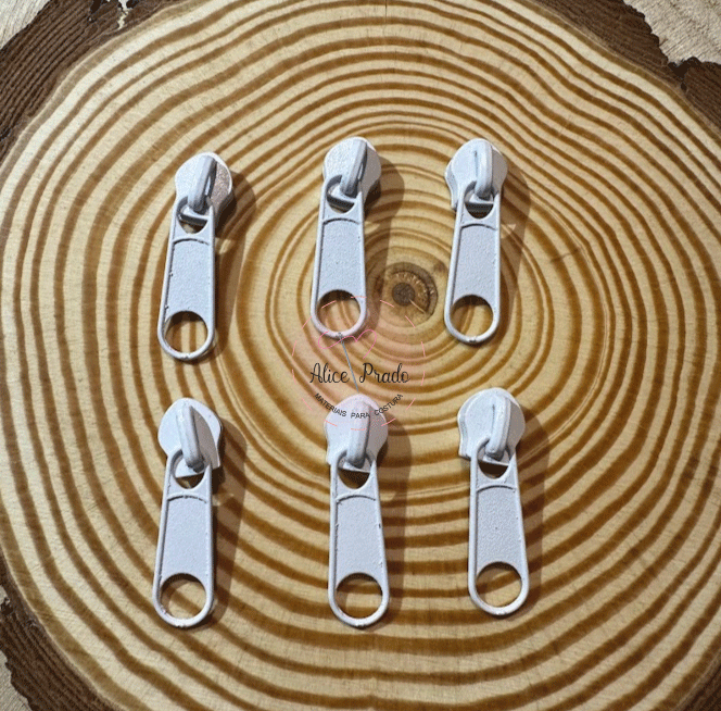 Seis cursores de zíper brancos sobre madeira clara com textura em anéis