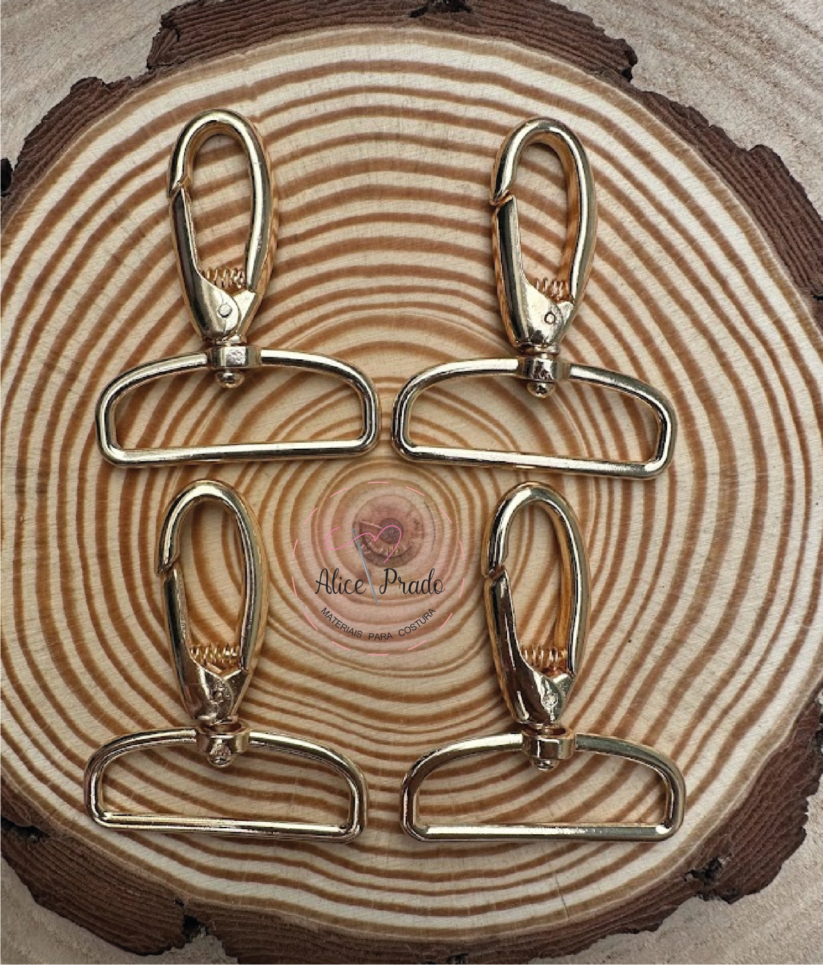 Quatro mosquetões dourados sobre superfície de madeira com selo Alice Prado