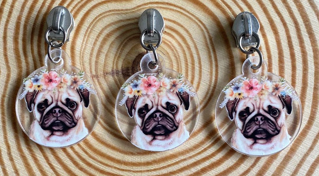 Três chaveiros de pug com coroas de flores em fundo de madeira