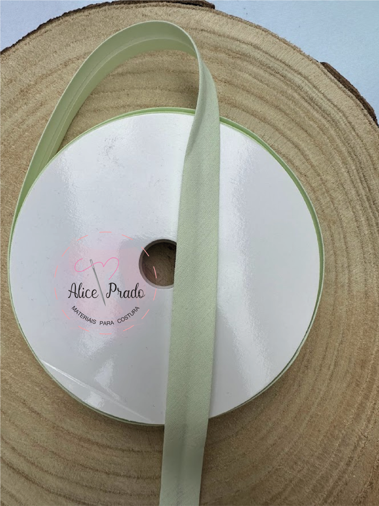Rolo de fita têxtil verde claro com etiqueta Alice Prado sobre superfície de madeira