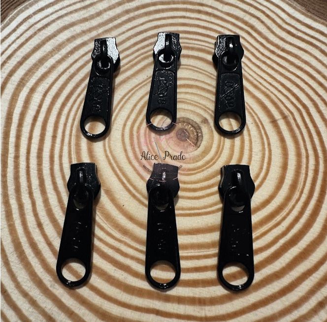 Seis puxadores de zíper pretos sobre superfície com padrão de círculos concêntricos em tons de bege e castanho