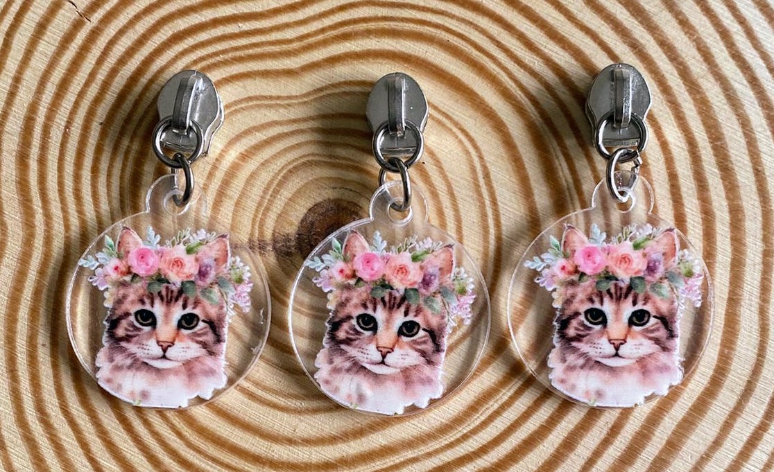 Três porta-chaves transparentes com imagem de gato com coroa de flores sobre superfície de madeira