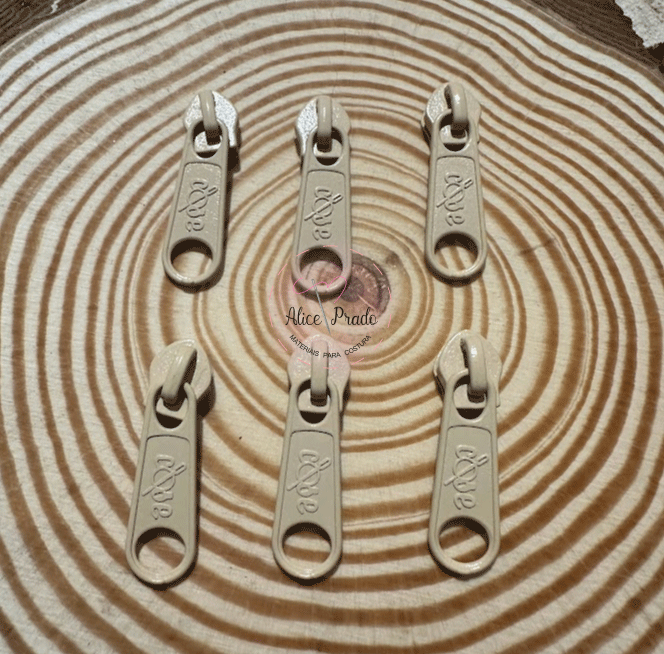 Seis pegas de fecho éclair bege sobre superfície de madeira com padrão de anéis