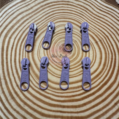 Oito puxadores de zíper lilás em superfície de madeira com anéis circulares