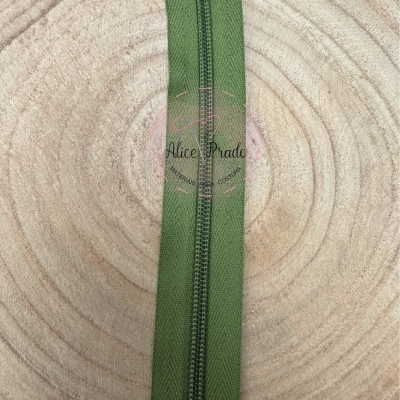 Fecho éclair verde sobre madeira clara com selo vermelho Alice Prado