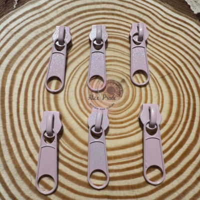 Seis puxadores de zíper rosa claro em superfície com padrão de anéis concêntricos