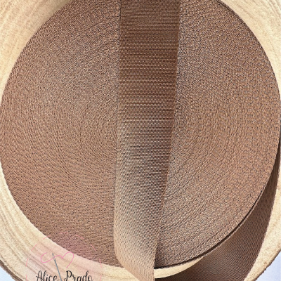 Rolo de fita textil castanha com textura dentro de recipiente cilíndrico claro.