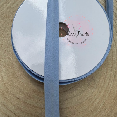 Rolo de fita de tecido azul claro com etiqueta branca sobre superfície de madeira redonda