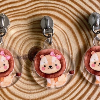 Três chaveiros de leão com laço rosa em fundo de madeira com anéis concêntricos
