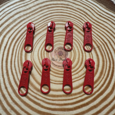 Cursoras de fechar de correr vermelhas sobre madeira com etiqueta 'Alice Prado'