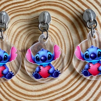 Três chaveiros transparentes com personagem Stitch segurando um coração vermelho sobre padrão espiral bege